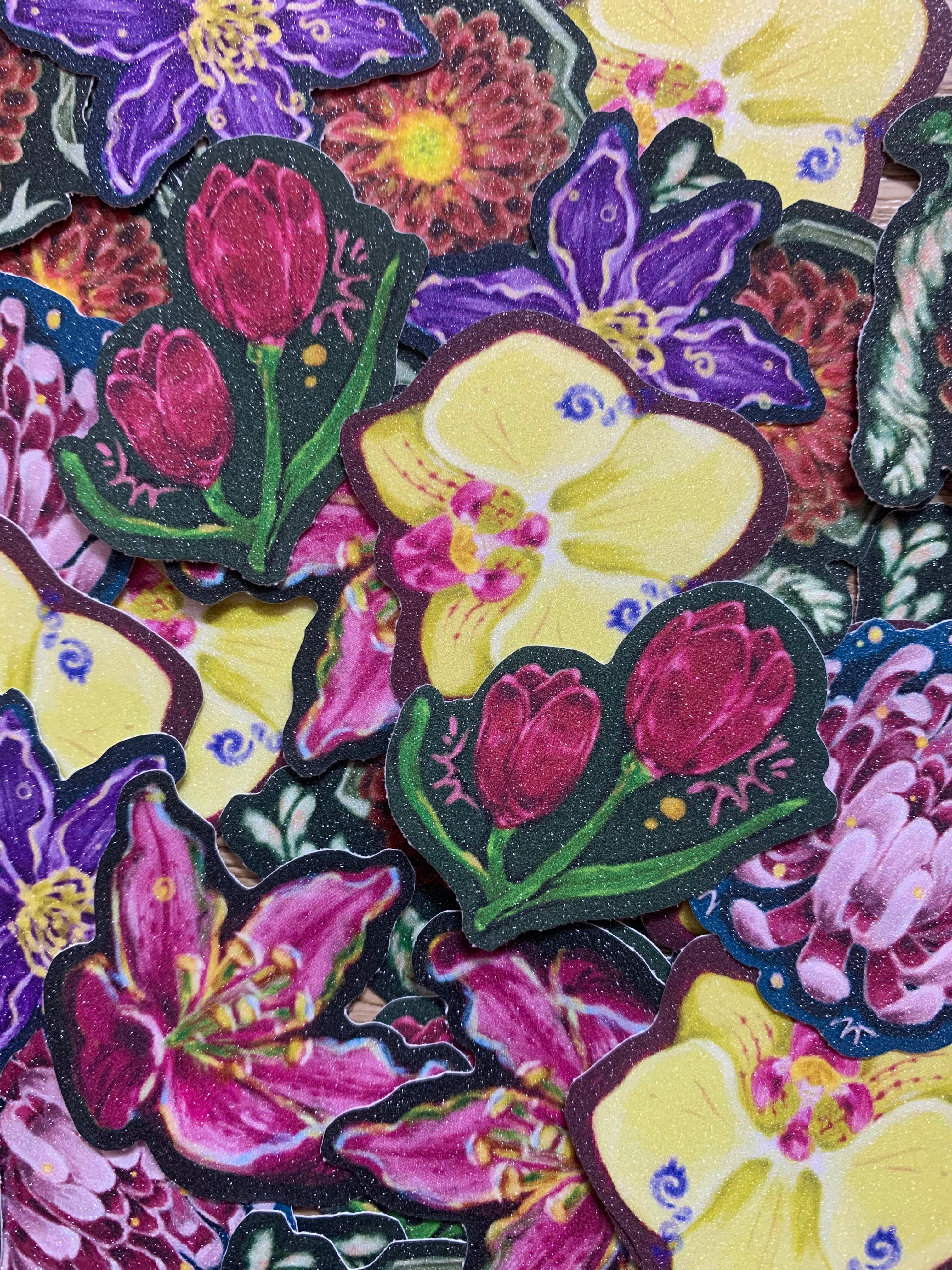 A close-up pile of die-cut featuring colorful floral designs, including yellow orchids, purple flowers, pink lilies, and red tulips with green leaves.